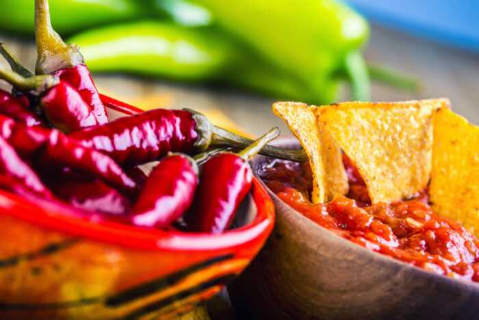 Colorful Chattanooga spicy Mexican food and peppers sitting in a red boal next to a grey bowl filled with spicy salsa and chips.